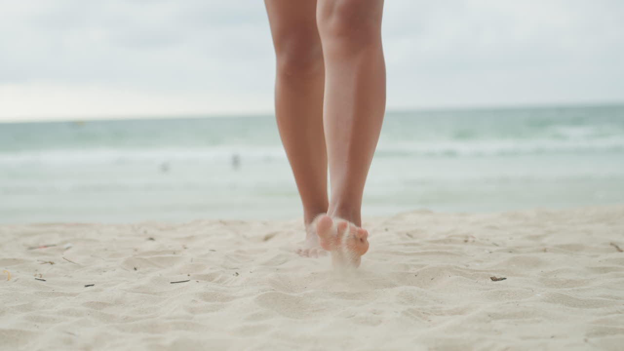 Donna pacifica che passeggia lungo una spiaggia serena. Donna delicata che si gode udibilmente la tranquilla mattina sulla riva sabbiosa. Signora tranquilla a piedi nudi che passeggia in una mattina pacifica in riva al mare calmo.