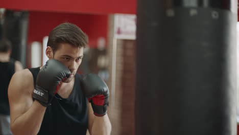 Fitness-man-in-gloves-making-blows-on-combat-bag-at-boxing-training-in-gym.