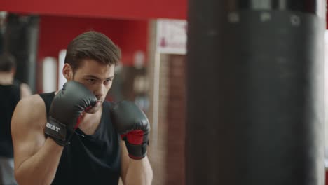 Fitness-Mann-In-Handschuhen,-Der-Beim-Boxtraining-Im-Fitnessstudio-Schläge-Auf-Die-Kampftasche-Ausführt.