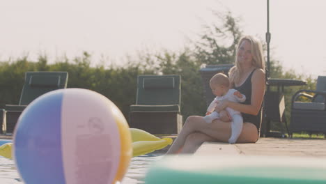 mother with baby daughter having fun on summer vacation  sitting by outdoor swimming pool