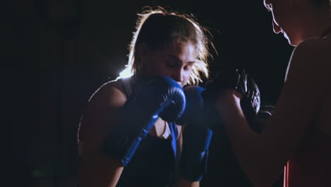 medium shot of beautiful fitness woman boxer treneruemsya strike speed focus mitts with a coach in a boxing club. slow motion