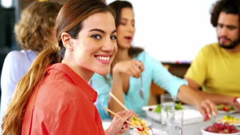 retrato de una mujer almorzando mientras un colega interactúa en el fondo