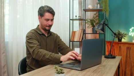 middleaged man smiling rubbing hands viewing laptop report celebrates big profitable deal at table