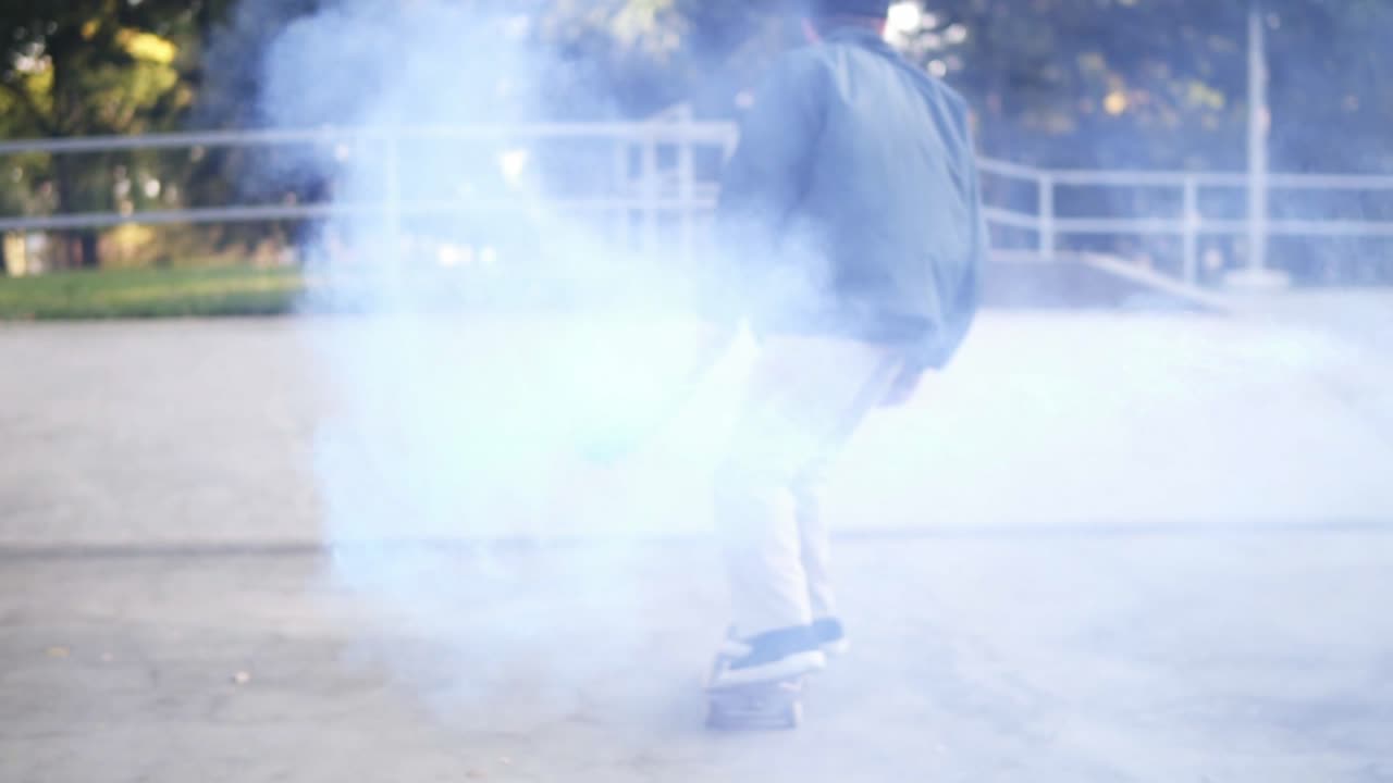 화창한 여름날 스케이트 램프에서 파란 색의 타는 연기 폭탄을 들고 연습하는 젊은 남자