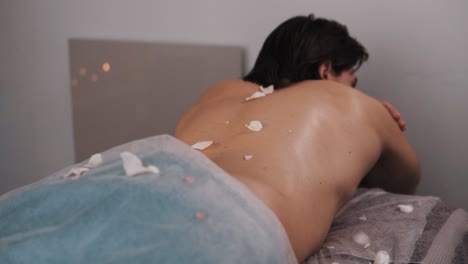 close-up handsome athletic man lying on a massage table with flower petals on his back prepares for an aromatherapy massage