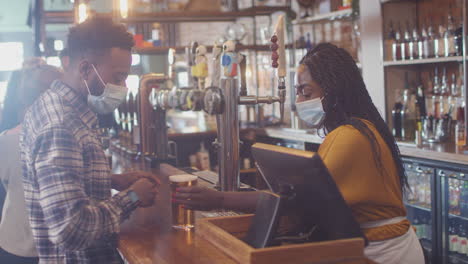 Male-Customer-Wearing-Mask-In-Bar-Making-Contactless-Payment-For-Drinks-During-Health-Pandemic