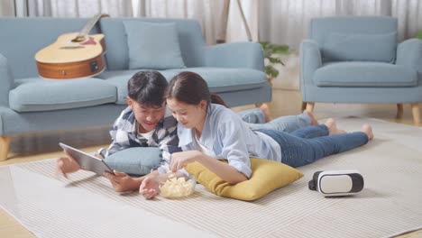 집에서 바닥에 카에 누워있는 동안 태블릿을 사용하는 아시아 십대 커플의 몸이 가득 차 있습니다. 영화를 보고 간식을 먹고, 이야기하고, 함께 시간을 즐기고 있습니다.