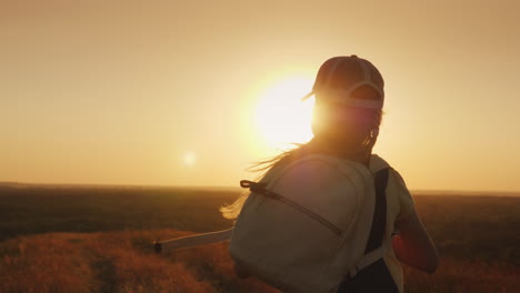 un niño de pelo largo con una mochila corre hacia el sol, los sueños de los niños y el concepto de vacaciones