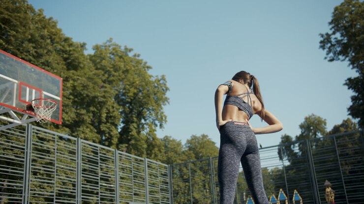 Vista traseira de uma mulher esportiva aquecendo e alongando em quadra de basquete ao ar livre em uma manhã de verão