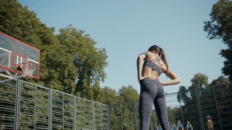 vista trasera de una mujer deportiva calentándose y estirándose en una cancha de baloncesto al aire libre en una mañana de verano