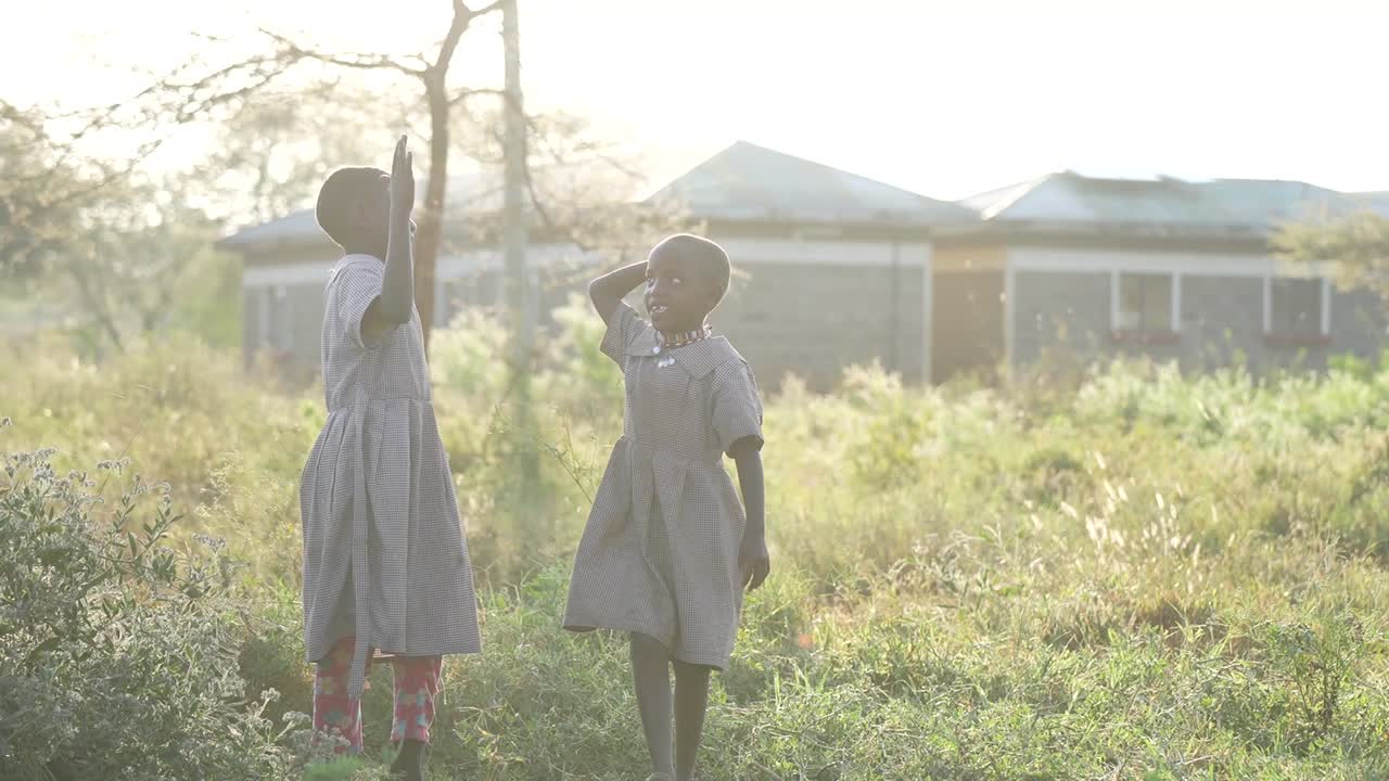 Young girls playing together in an African school playground, joyful happiness as they walk side by side holding hands and laughing