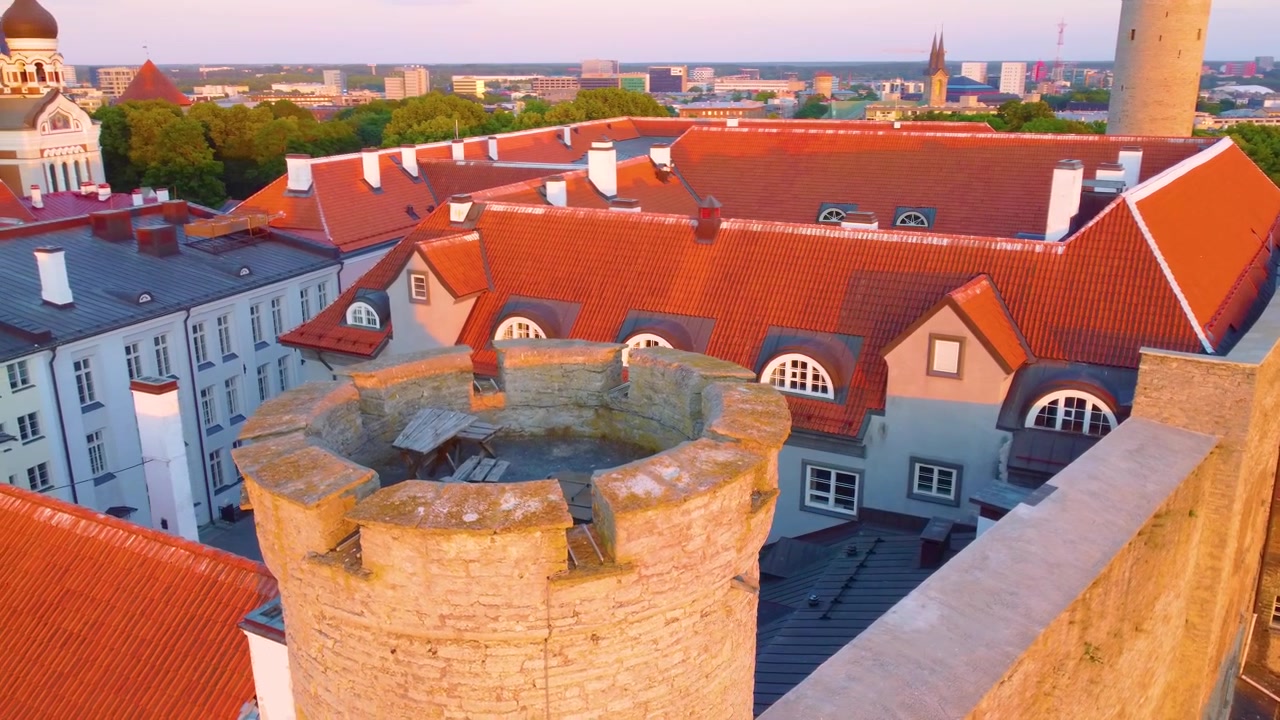 Vista panoramica della Città Vecchia di Tallinn, caratterizzata da architettura storica, tetti in tegole rosse e una torre medievale in pietra sotto un cielo al tramonto.
