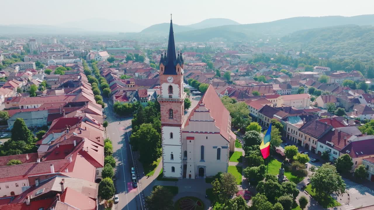 A aerial drone captures the historic tower of the Evangelical Church in Bistrita, showcasing the surrounding European city center, full of traditional buildings with forested mountains in the distance