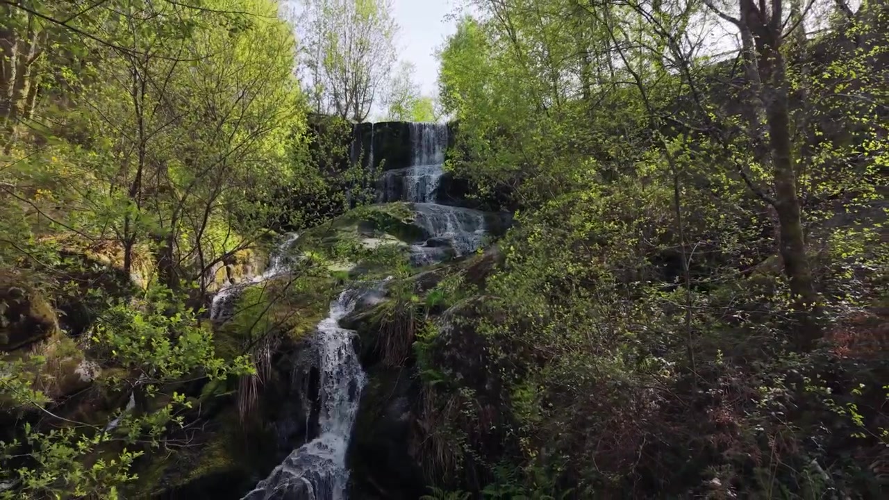 Cascata a più livelli circondata da fitta vegetazione verde presso le Cascate Fervenza da Ruxida in Galizia, Spagna. Ripresa aerea con allontanamento
