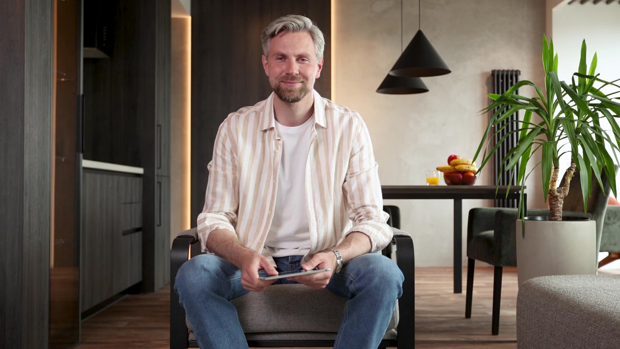 Glad mand vinker og smiler under videoopkald på tablet derhjemme