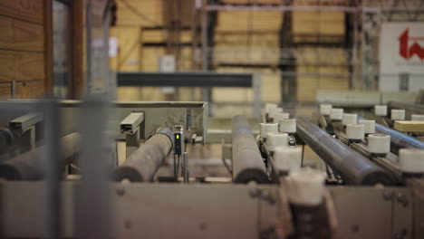 timber logs stacked in large warehouse interior of industrial wood processing plant as single planks pass over conveyor belt