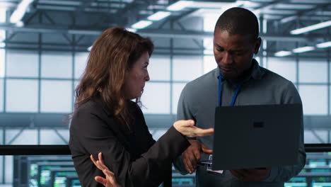 Developers in data center workspace coding on laptop, analyzing metrics