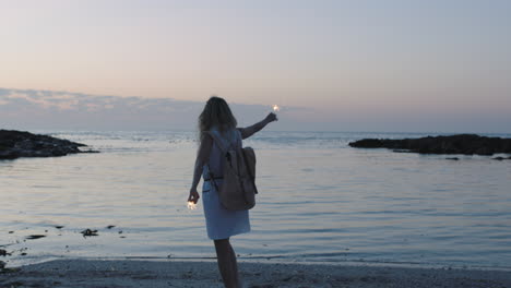 Porträt-Einer-Jungen-Frau-Mit-Erhobenen-Wunderkerzen,-Die-Am-Friedlichen-Strand-Spaziert-Und-Abenteuer-Feiert