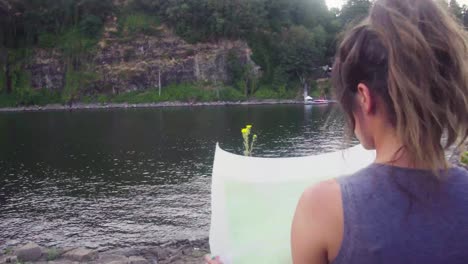 cute hipster girl unrolling a paper map on the edge of water in a park