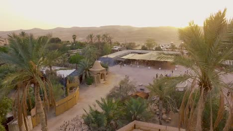 happy village in the desert with palm trees during sunset with people walking across