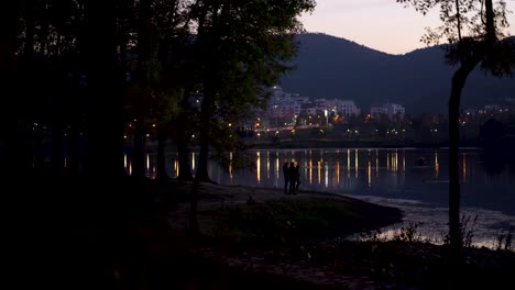 Parque-De-La-Ciudad-Alrededor-De-Un-Lago-Tranquilo-Que-Refleja-Las-Luces-De-La-Calle-En-Aguas-Tranquilas-Al-Atardecer