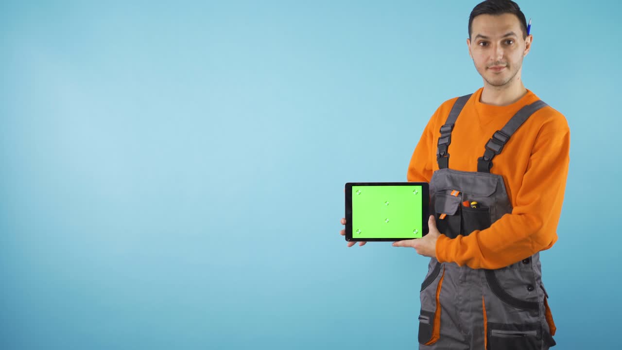 joven artesano con ropa de trabajo sosteniendo una tableta de pantalla verde con espacio vacío