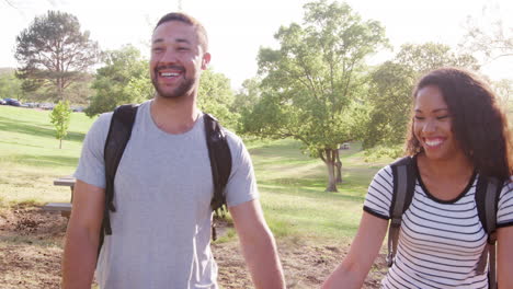 slow motion shot of couple wearing backpacks hiking in park together