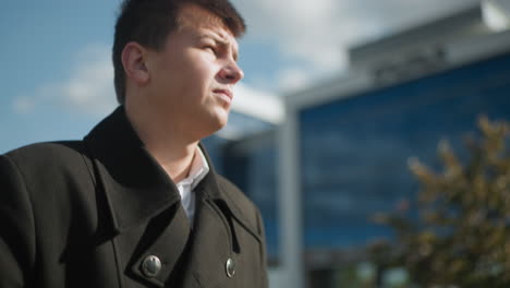 close-up of elegant black coat with shiny metallic buttons in outdoor urban setting as individual checks time on wristwatch, blurred background includes modern buildings, and parked cars