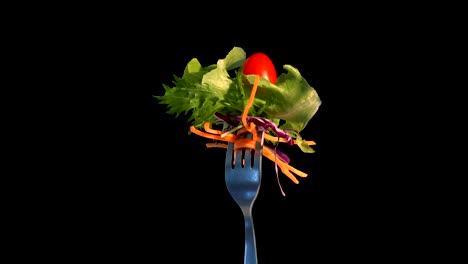 comida de ensalada de verduras en el tenedor sobre fondo negro.