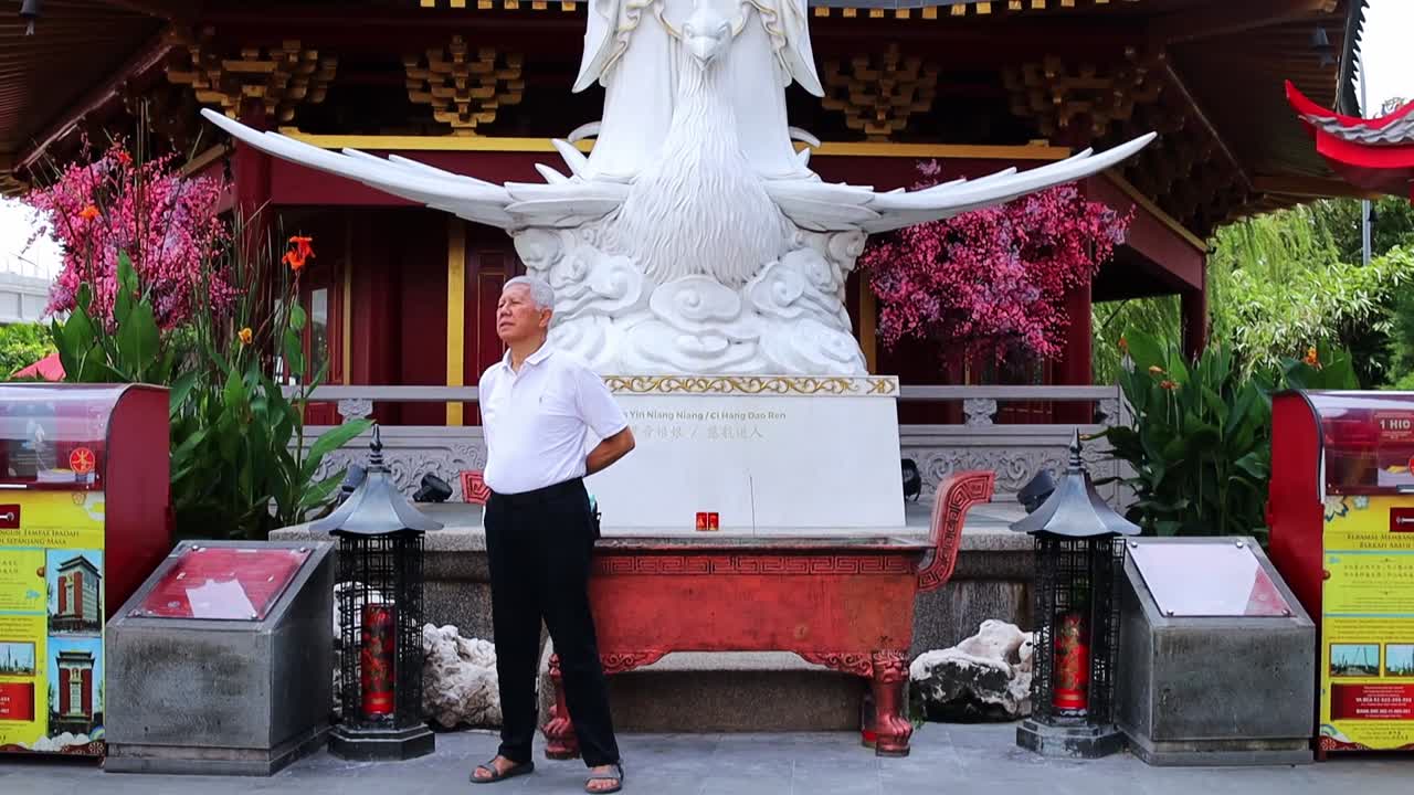 Ældre kinesisk mand, der står foran statuen af Guan Yin Niang Niang eller Ci Hang Dao Ren i et asiatisk tempel