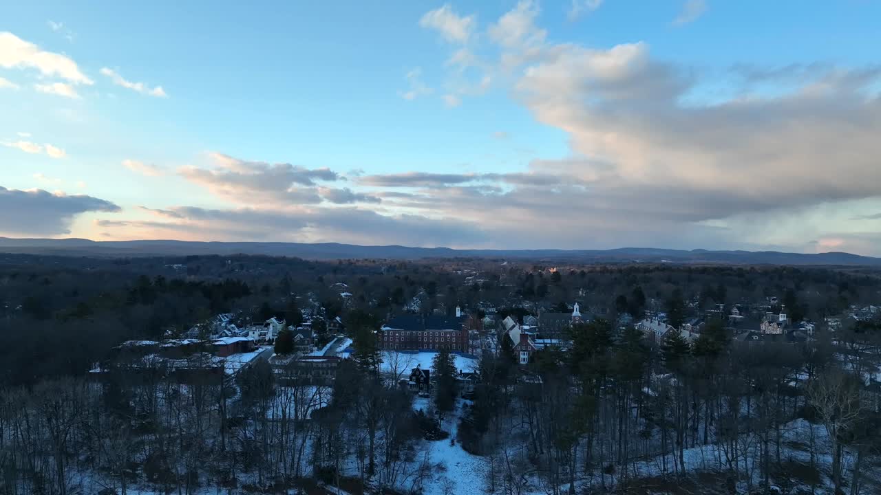 Stunning drone footage showcasing the snowy town of Northampton at sunset, with tree-covered landscapes and distant mountains under a vibrant sky.