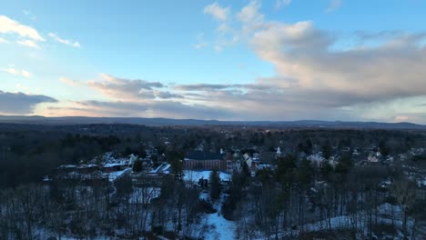 stunning drone footage showcasing the snowy town of northampton at sunset, with tree-covered landscapes and distant mountains under a vibrant sky.