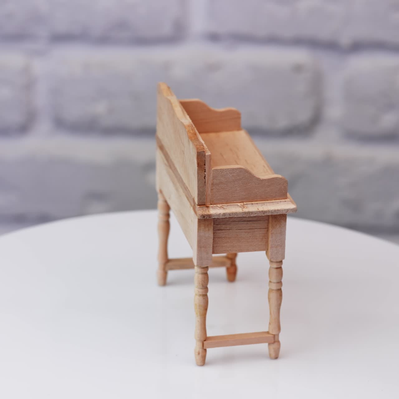 Miniature wooden table with a drawer at the spinning table. High angle view at white brick wall backdrop. Close up