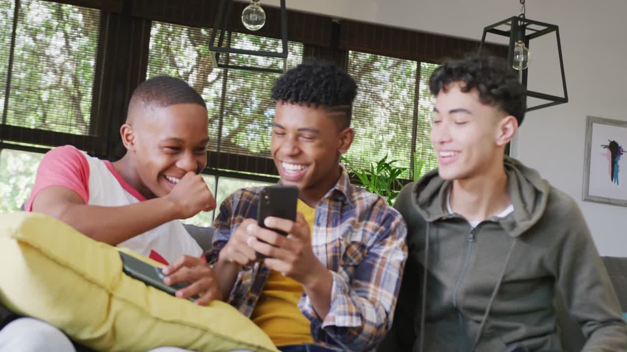Video of happy diverse male teenage friends using smartphones, slow motion
