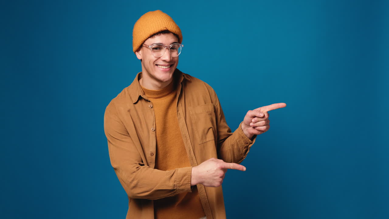A smiling man in a beanie and glasses pointing to the right
