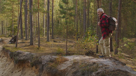 middle-aged-man-is-walking-on-high-shore-of-river-in-forest-at-autumn-day-ecotourism-and-fishing-at-travel-and-vacation