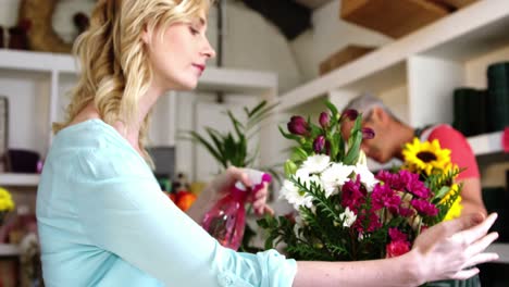 female florist spraying water on bunch of flowers in flower shop