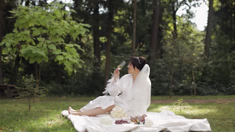 wedding bride in boudoir dress sitting in morning garden drinking champagne woman in night gown veil