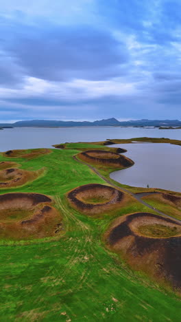 volcanic craters in myvatn lake, iceland. pseudo craters on a grassy field under the cloudy sky. vertical video.
