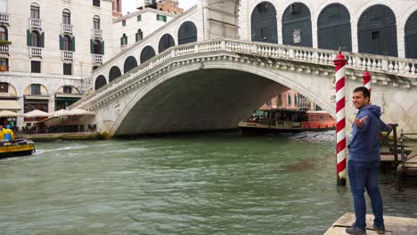 Glücklicher-Mann-Posiert-In-Ponte-Rialto-Neben-Einem-Kanal-In-Venedig-Mit-Einer-Bootsüberfahrt