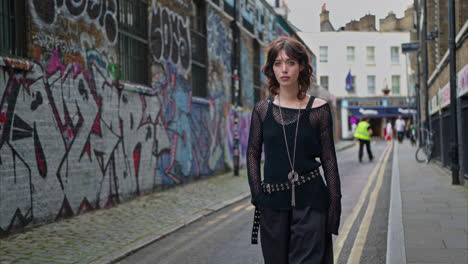 outdoor-mode-porträt einer jungen alternative-stil-frau, die in london city street, großbritannien, in echtzeit an graffiti bedeckten wänden vorbeigeht