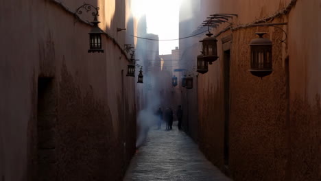 People walking through a smoky, lantern-lit alleyway in a historic town