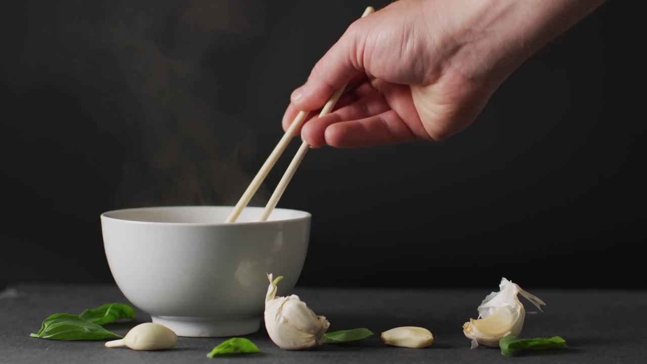 Hand holding chopsticks with noodles in bowl on black background