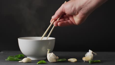 Hand-holding-chopsticks-with-noodles-in-bowl-on-black-background