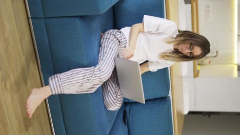Blonde-woman-in-pajama-sit-on-the-couch-and-opens-the-silver-laptop
