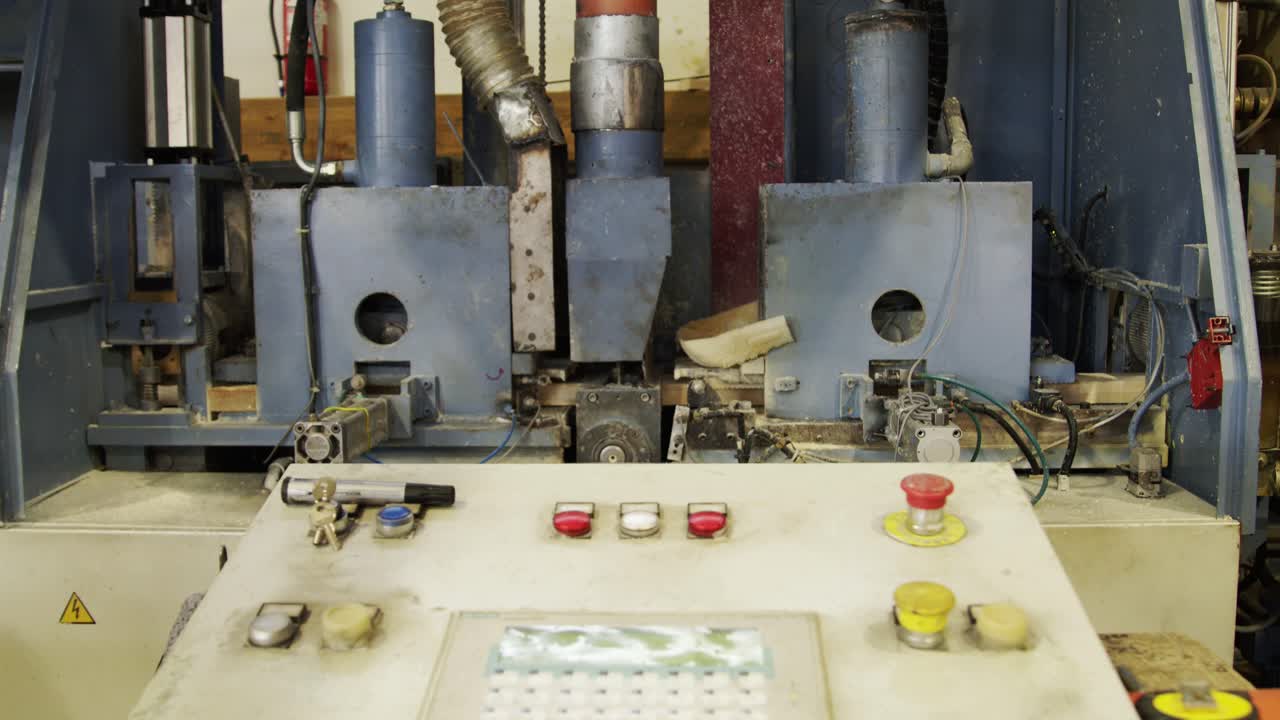 An automated machine completes a manufacturing cycle in a modern factory. A wooden block is fed, processed by sanders or cutters, and ejected, with the control panel in the foreground