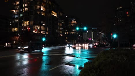 cars going straight ahead and waiting to turn left and right on an wet intersection where traffic light is switching between red, orange and green light in downtown vancouver