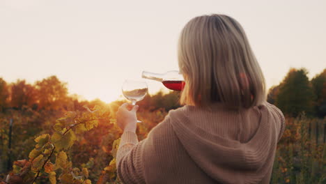 A-woman-pours-red-wine-into-a-glass.-It-stands-near-the-vineyard-at-sunset.-Tasting-and-wine-tour-concept