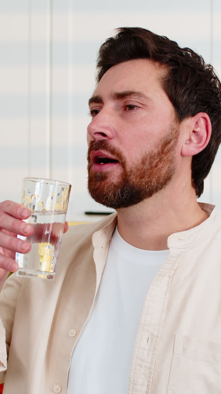 Homem de meia-idade despeja água fresca em um copo na cozinha de casa para representar o conceito de bem-estar, hidratação e dieta.