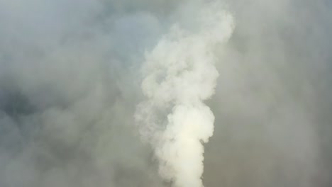 smoke from a power station chimney rising from a low, creeping fog. drone view